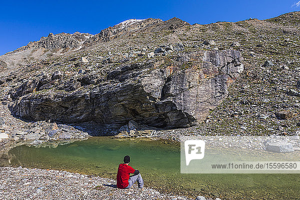 A hiker relaxes beside a pool of water in the Alaska Range; Alaska  United States of America