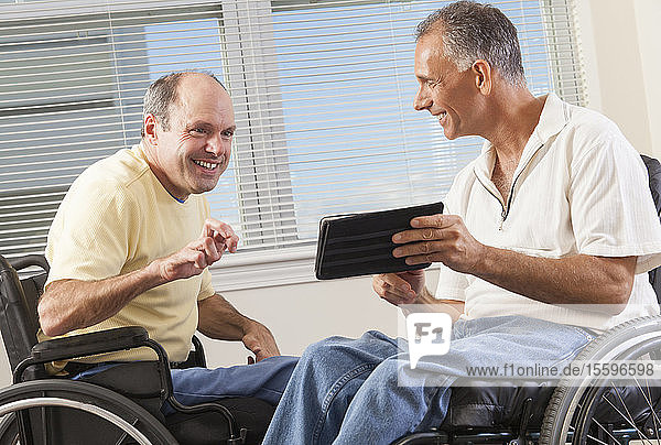 Zwei behinderte Männer sitzen in Rollstühlen und schauen auf ein digitales Tablet