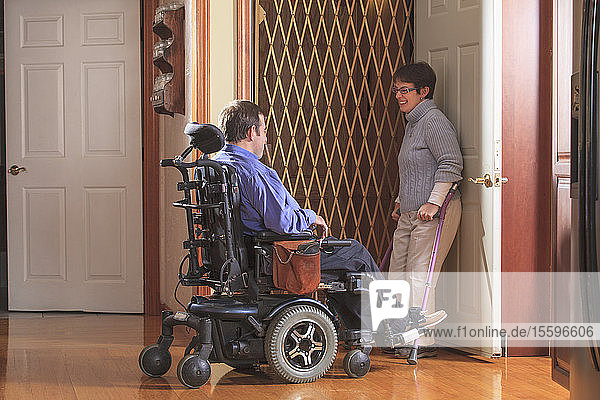 Frau mit Cerebralparese hilft Mann mit Cerebralparese im motorisierten Rollstuhl in den Hausaufzug