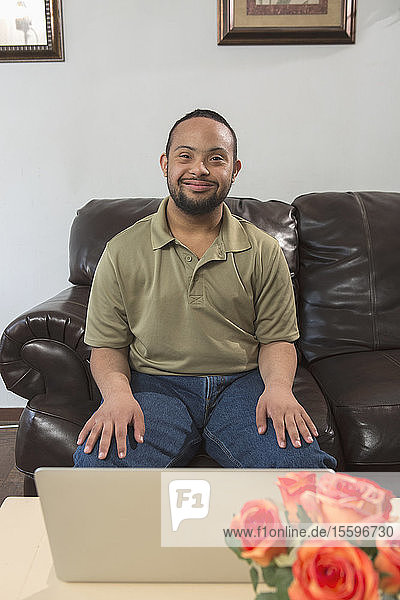 Glücklicher afroamerikanischer Mann mit Down-Syndrom  der zu Hause einen Laptop benutzt