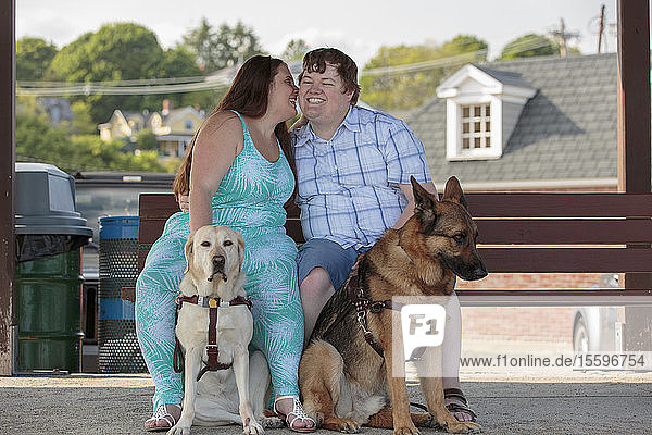 Young couple with visual impairments and service dogs sitting on a bench and telling a secret