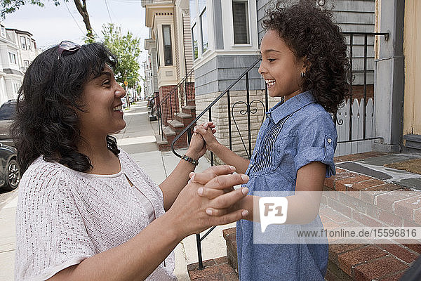 Hispanische Frau spielt mit ihrer Tochter vor ihrem Haus