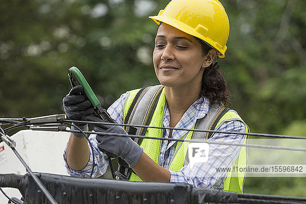 Hispanic female cable lineman crimping the cables in bucket lift
