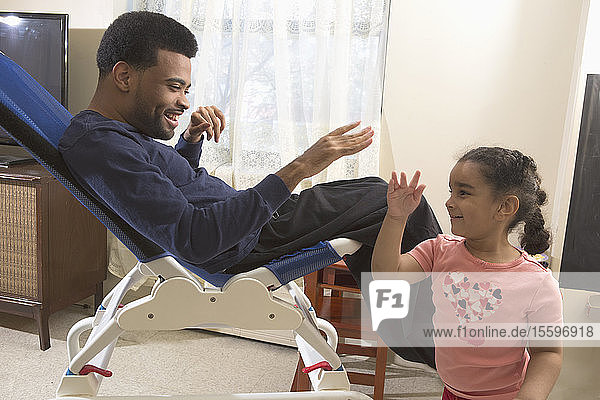 Glücklicher afroamerikanischer Mann mit zerebraler Lähmung  der mit seiner Tochter zu Hause spielt