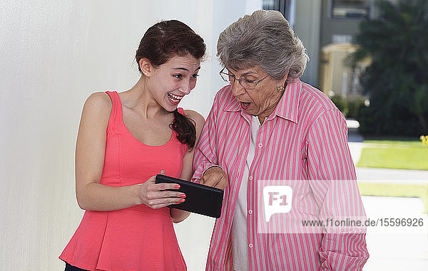 Lächelnde ältere Frau und ihre Enkelin  die ein digitales Tablet benutzt