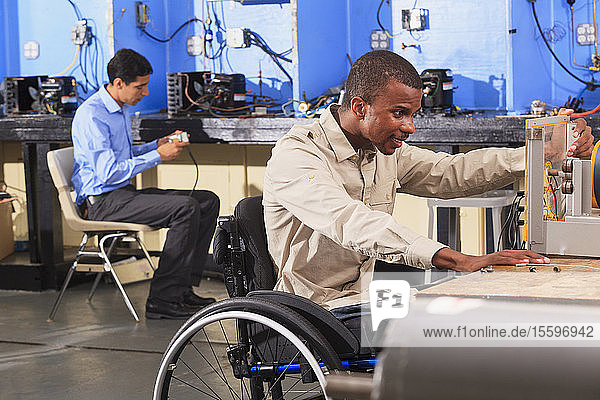 Ein Student im Rollstuhl baut ein Generator-Experiment auf  während ein Student das HLK-System untersucht