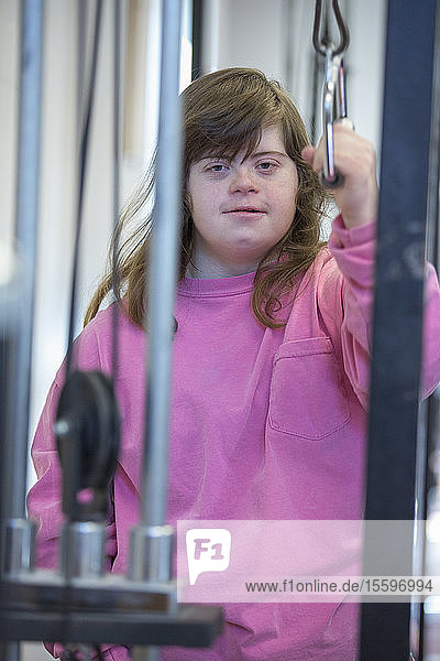 Junge Frau mit Down-Syndrom bei der Arbeit an einem Trainingsgerät im Fitnessstudio
