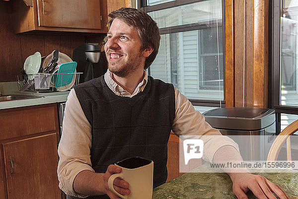 Junger blinder Mann sitzt in seiner Küche mit einer Tasse Kaffee