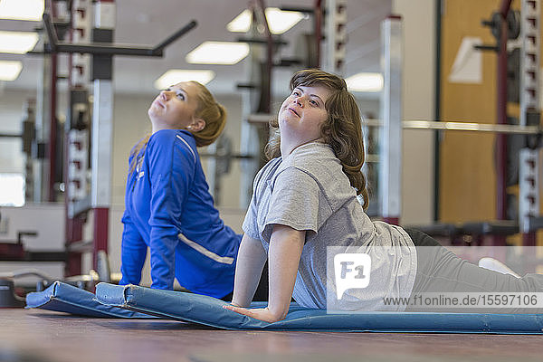 Junge Frau mit Down-Syndrom trainiert mit ihrem Trainer auf einer Übungsmatte im Fitnessstudio