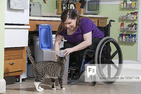 Frau mit Spina Bifida im Rollstuhl füttert eine Katze in der barrierefreien Küche
