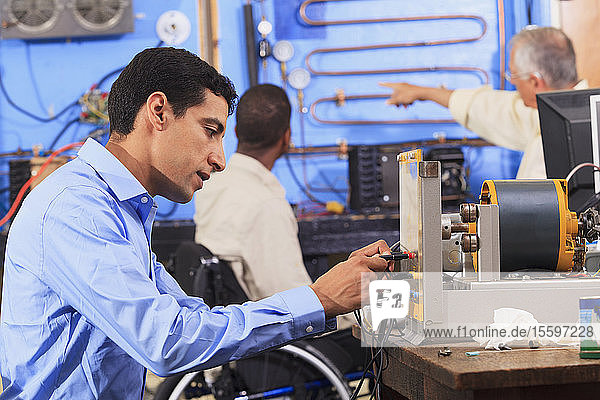 Ein Schüler baut ein Generator-Experiment auf  während der Ausbilder einem Schüler im Rollstuhl das HLK-System erklärt