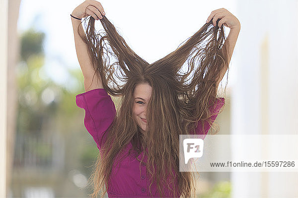 Lächelnde junge Frau hält ihr langes Haar in die Luft