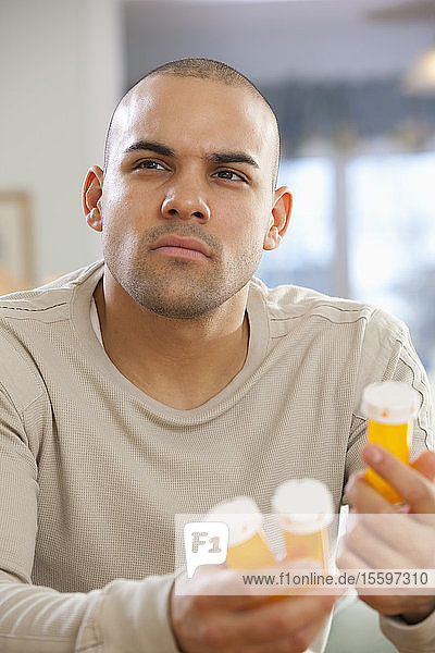Hispanischer Mann hält Pillenflaschen und denkt nach