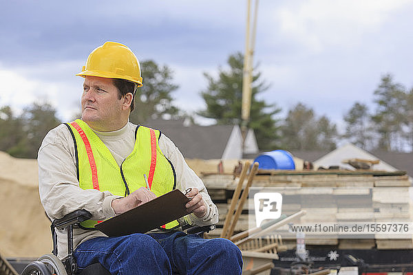 Construction supervisor with Spinal Cord Injury taking notes with concrete foundation forms in background