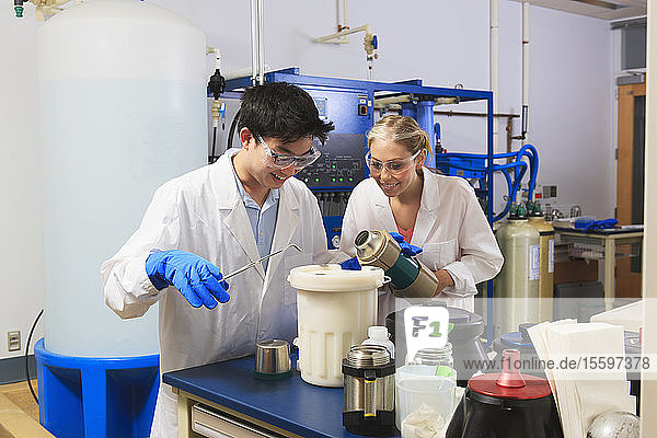 Engineering students using forceps while holding liquid nitrogen Dewar flask in water processing room in a laboratory
