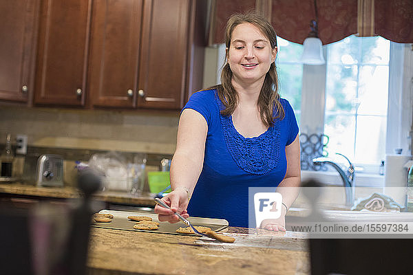 Junge Frau mit zerebraler Lähmung legt Kekse auf ein Tablett