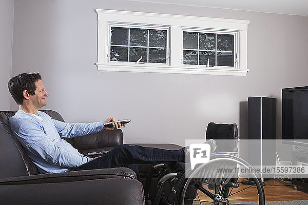 Mann mit Rückenmarksverletzung und Bein im Rollstuhl sieht mit Fernbedienung fern