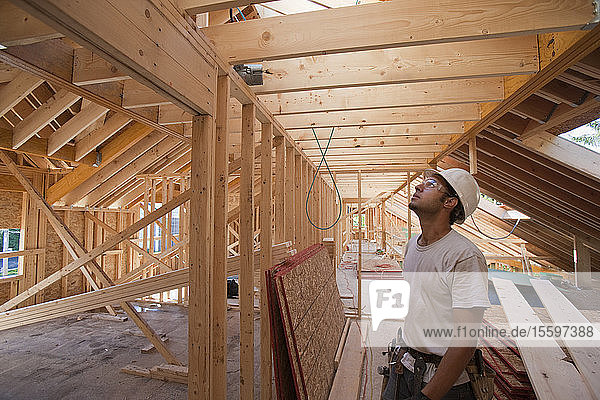 Hispanischer Zimmermann betrachtet das Dach im Obergeschoss eines im Bau befindlichen Hauses