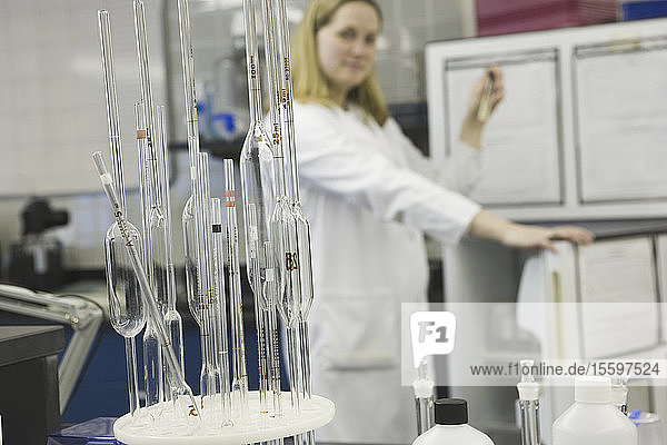 Nahaufnahme von volumetrischen Pipetten in einem Pipettenständer mit einer Wissenschaftlerin im Hintergrund in einem Labor
