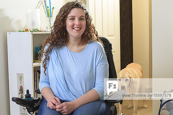 Frau mit Muskeldystrophie in ihrem Elektrorollstuhl mit ihrem Diensthund hinter ihr