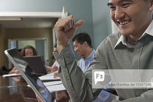 Geschäftsmann  der einen Laptop benutzt  mit seinen Kollegen im Hintergrund in einem Sitzungssaal