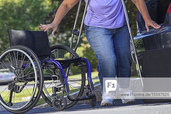 Frau mit Spina Bifida sitzt im Rollstuhl  nachdem sie ihn außerhalb des Autos zusammengebaut hat