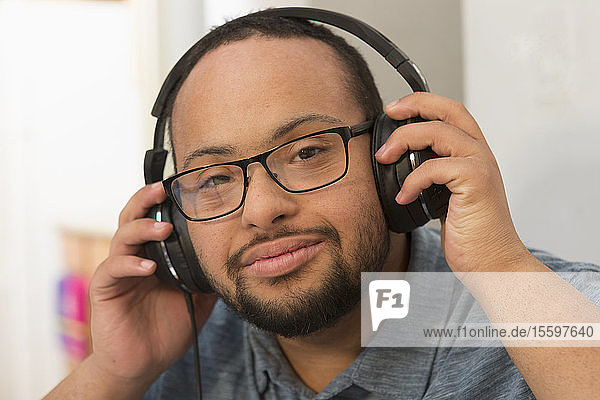 Glücklicher afroamerikanischer Mann mit Down-Syndrom  der zu Hause mit Kopfhörern Musik hört