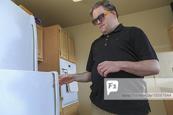 Man with congenital blindness using the refrigerator in his kitchen