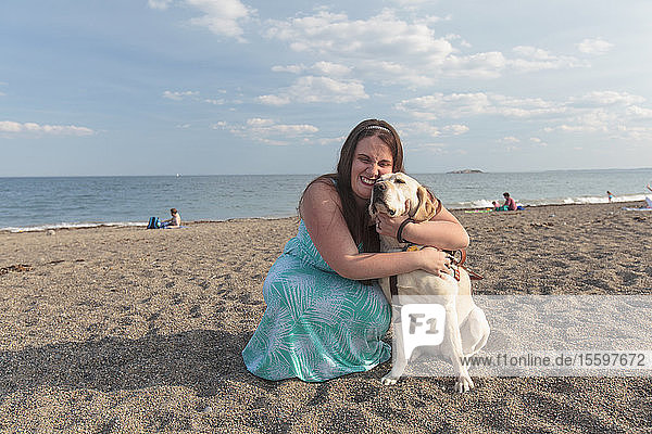 Junge Frau mit Sehbehinderung und ihr Diensthund umarmen sich am Strand