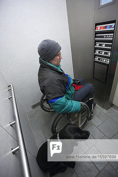 Frau mit Multipler Sklerose benutzt einen Aufzug mit einem Diensthund