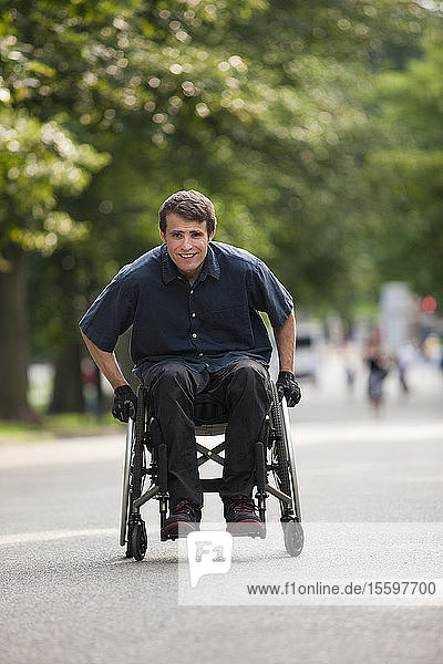 Mann mit Rückenmarksverletzung im Rollstuhl  der den Rollstuhl schnell auf einem Weg durch einen öffentlichen Park manövriert