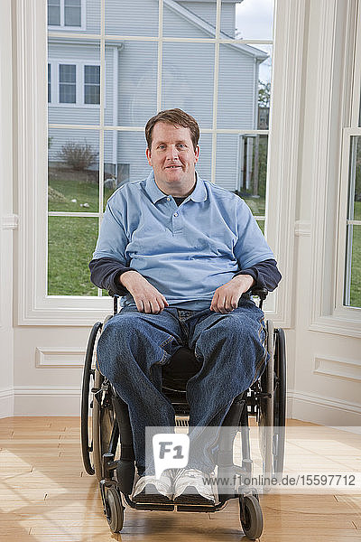 Mann mit Rückenmarksverletzung im Rollstuhl lächelt in seinem barrierefreien Haus