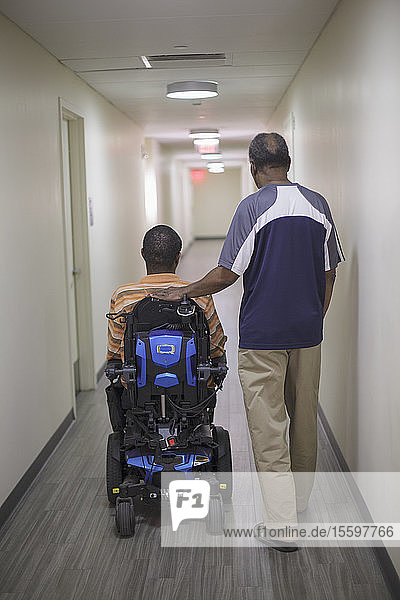 Mann mit Guillain-Barre-Syndrom im Wohnungsflur auf einem elektrischen Stuhl mit seinem Vater
