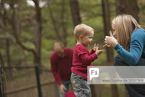 Frau  die das Wort Play in amerikanischer Gebärdensprache gebärdet  während sie mit ihrem Sohn in einem Park kommuniziert