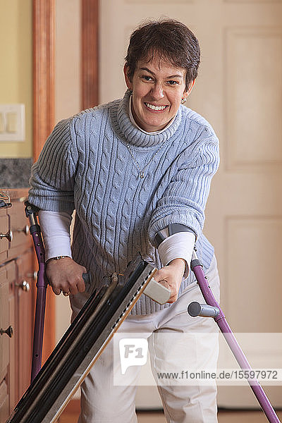 Frau mit Cerebralparese benutzt Krücken und öffnet ihren Ofen in ihrer Küche