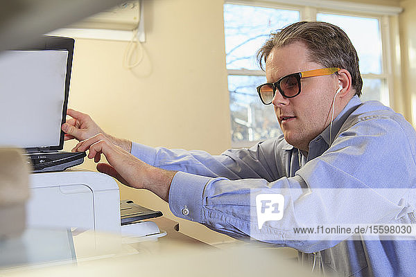 Mann mit angeborener Blindheit scannt Papierkram an seinem Computer
