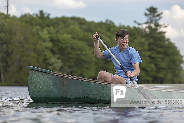 Junger Mann mit Down-Syndrom rudert ein Kanu auf einem See