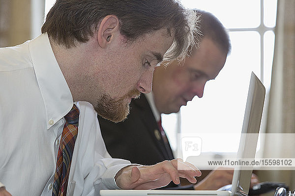 Mann mit Down-Syndrom arbeitet mit einem Mitarbeiter an einem Laptop im Büro des State Capitol