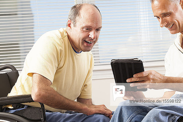 Zwei behinderte Männer sitzen in Rollstühlen und schauen auf ein digitales Tablet