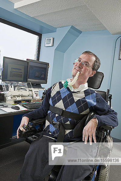 Geschäftsmann mit Duchenne-Muskeldystrophie  der ein Beatmungsgerät in einem Büro benutzt