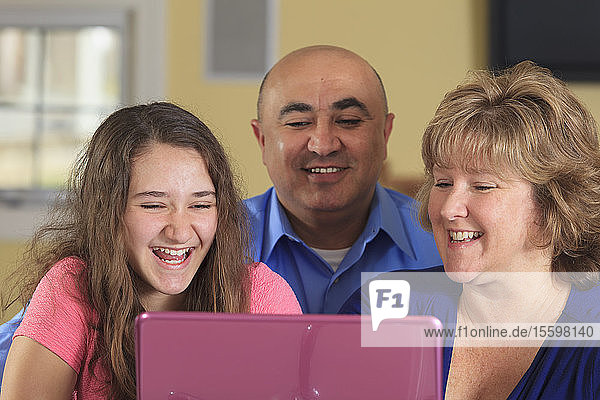 Tochter mit Vater und Mutter lachend am Laptop