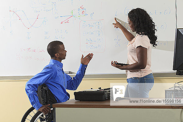 Zwei Studenten der Ingenieurwissenschaften  einer im Rollstuhl  diskutieren elektronische Gleichungen auf einem Whiteboard