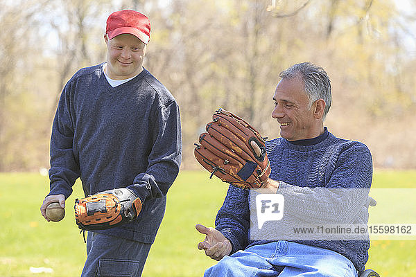 Vater mit Rückenmarksverletzung und sein Sohn mit Down-Syndrom spielen Baseball im Park