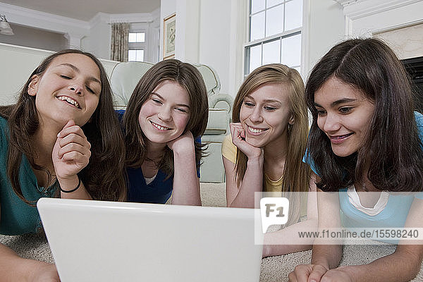 Zwei hispanische Mädchen im Teenageralter benutzen einen Laptop mit ihren Freunden