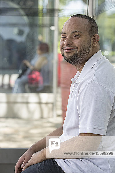 Mann mit Down-Syndrom sitzt an einer Bushaltestelle