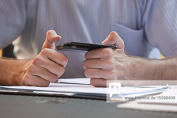 Geschäftsmann mit Friedreich-Ataxie  der mit einer degenerierten Hand Textnachrichten auf einem Mobiltelefon schreibt
