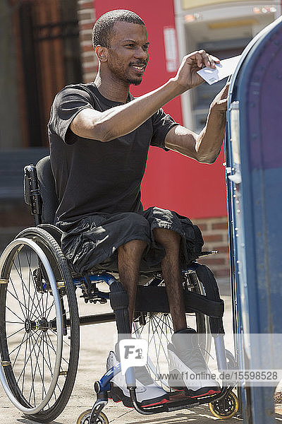 Mann im Rollstuhl  der an Spinaler Meningitis erkrankt ist  wirft einen Brief in einen öffentlichen Briefkasten