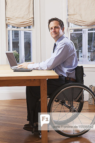 Geschäftsmann mit Querschnittslähmung im Rollstuhl bei der Arbeit am Laptop