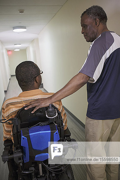 Mann mit Guillain-Barre-Syndrom im Wohnungsflur mit seinem Rollstuhl und seinem Vater