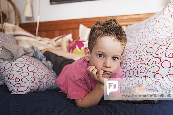 Porträt eines auf dem Bett liegenden Jungen mit seinem Smartphone